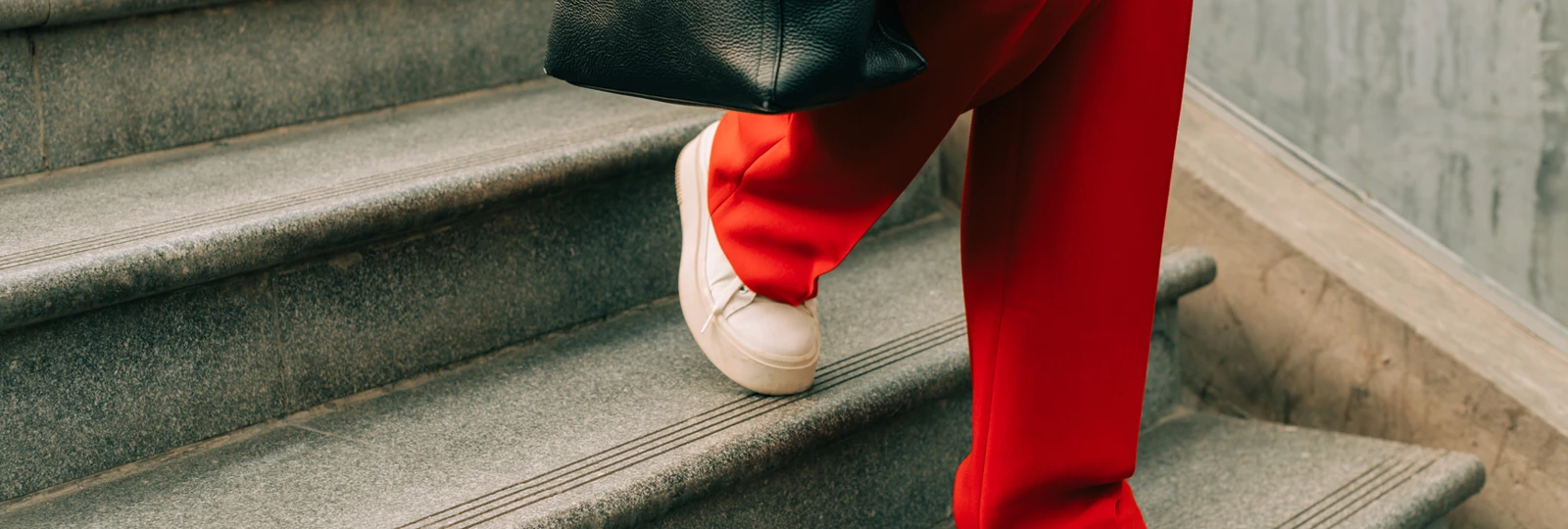woman wearing red trousers, wlaking down a set of stairs holding a bag